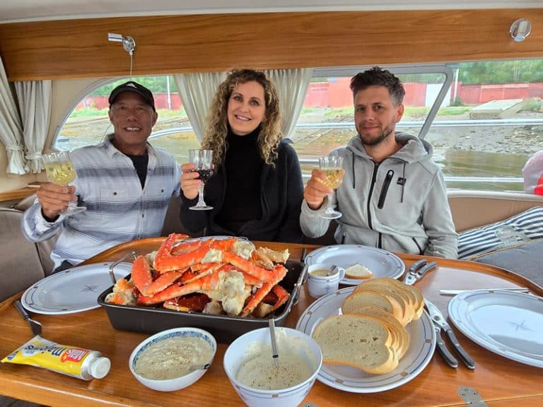Smiling guests eating freshly caught king crab on boat