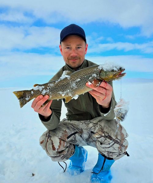male tourist holding fish on the ice