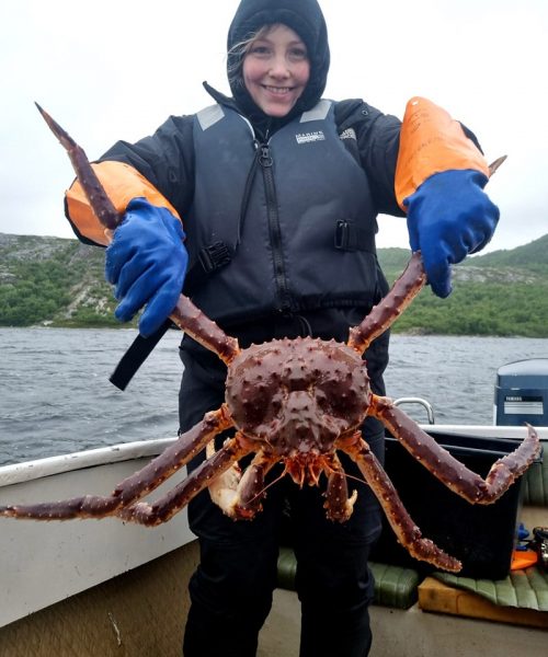 Smiling woman holding king crab on a boat